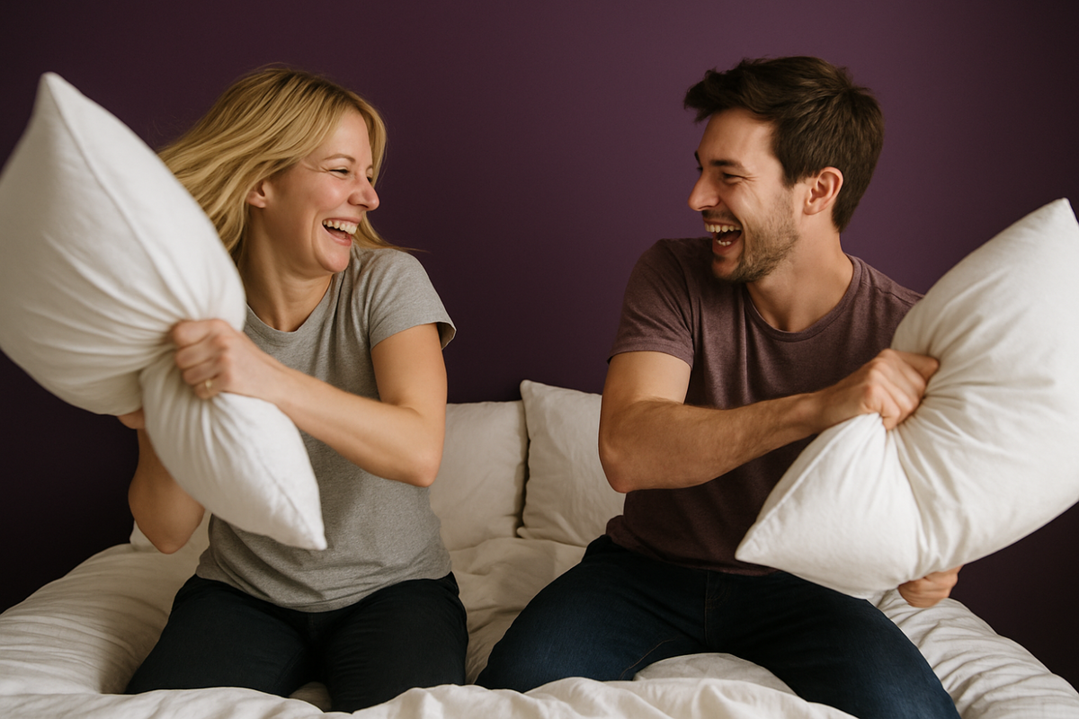 Couple enjoying pillow fight on comfortable bed with white pillows and bedding in modern bedroom setting. The bed is made with luxury bamboo sheets.