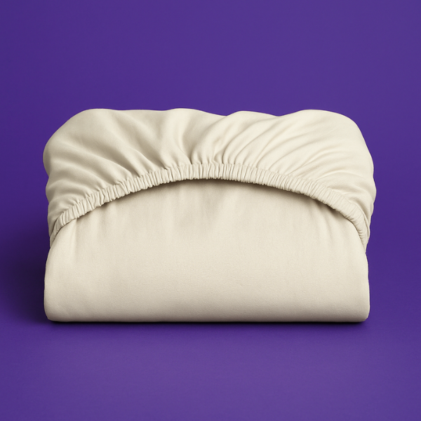 Premium cream-colored fitted sheet with elastic edge displayed on a vibrant purple background. The sheet features a smooth, wrinkle-resistant fabric with deep pockets and secure elastic banding that ensures a perfect fit on mattresses.