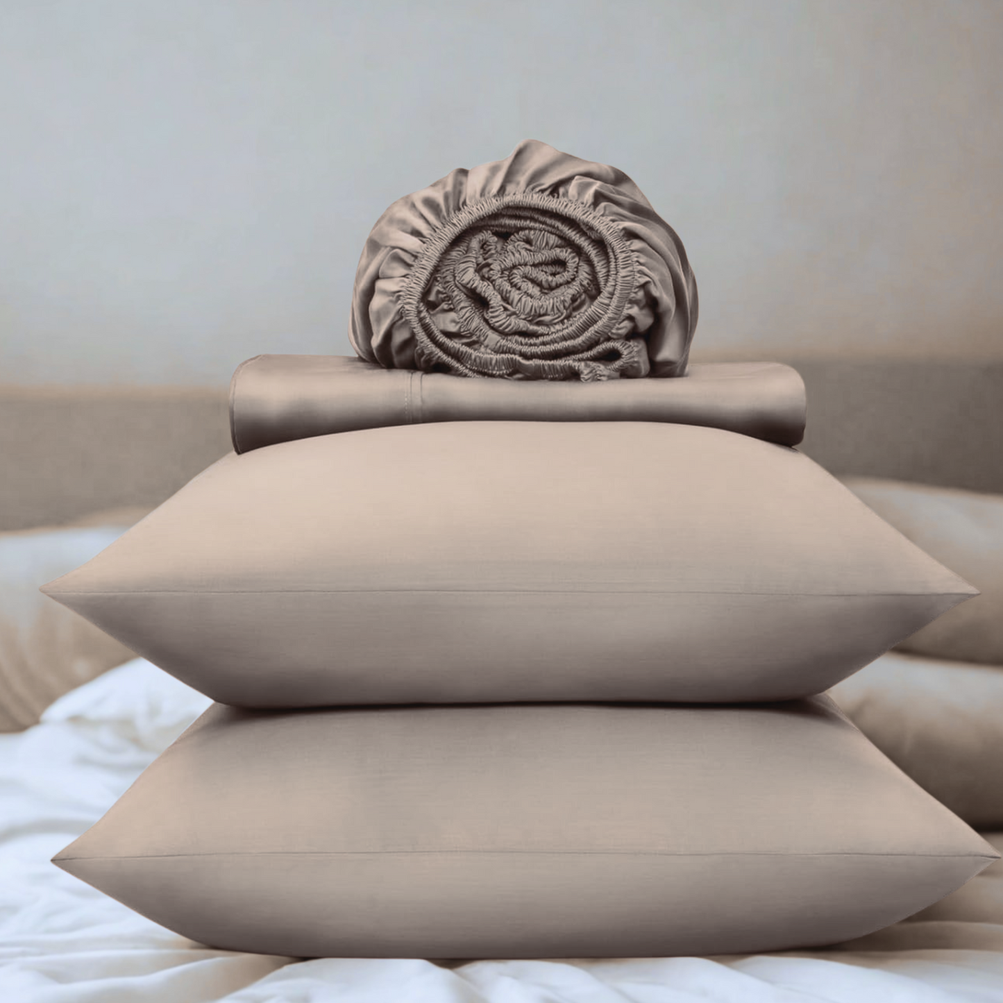 Beige pillows and folded blanket on a bed with a neutral background