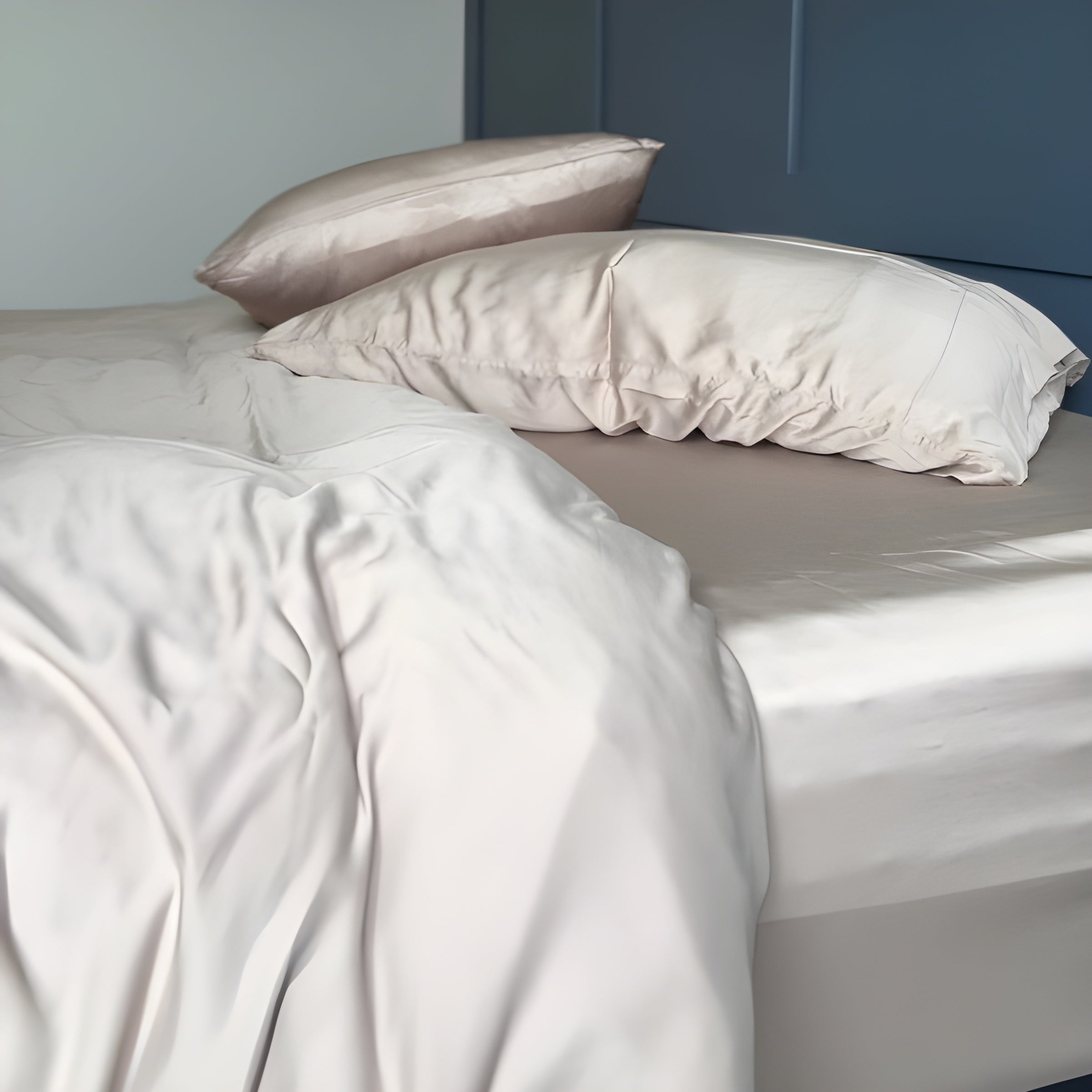 Neatly made bed with light-colored bedding and pillows against a neutral wall.