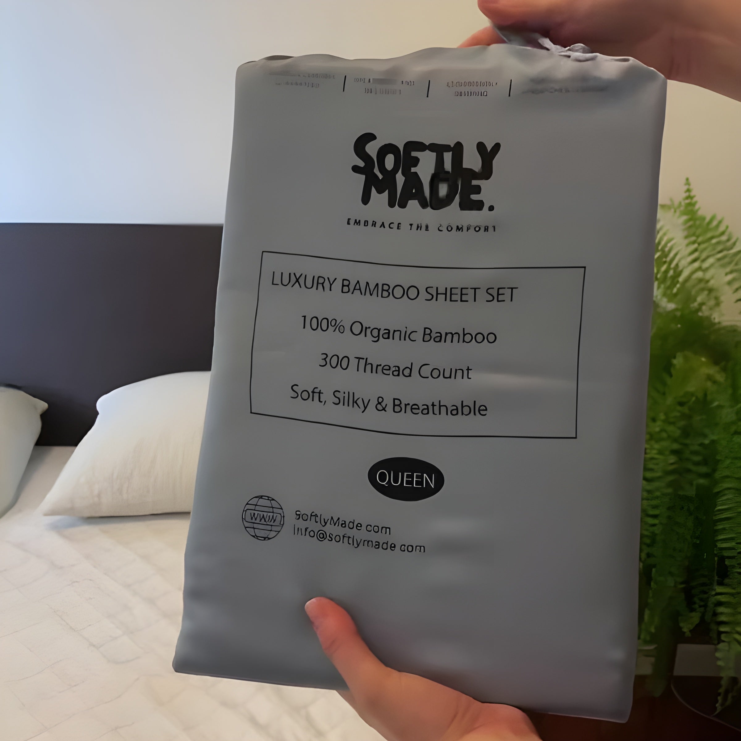 Package of Softly Made luxury bamboo sheet set held by a hand in a bedroom setting.