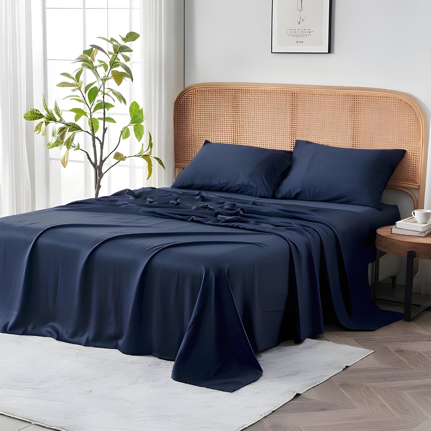 Luxurious navy blue bedding set elegantly styled on a bed with a natural rattan headboard in a bright, airy bedroom. The premium sheets showcase their smooth, flowing drape with subtle folds that highlight the fabric's exceptional quality. Two matching navy pillowcases rest against the textured headboard, creating a striking contrast.