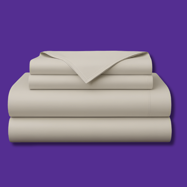 This image shows a neatly folded stack of cream-colored bed sheets on a vibrant purple background. The stack includes what appears to be a fitted sheet, flat sheet, and pillowcases. The sheets have a smooth, crisp appearance suggesting high-quality bedding. The top sheet has a folded corner revealing the edge detail.