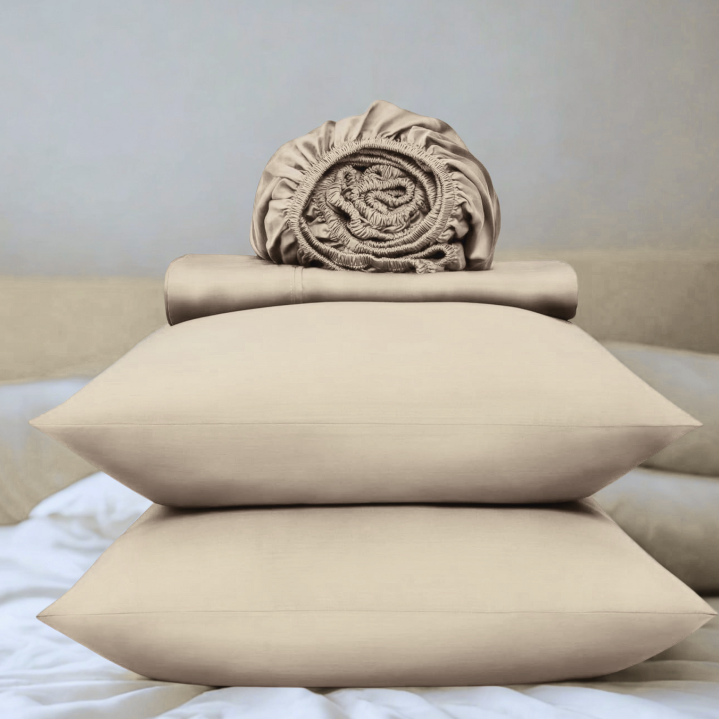 Beige pillows and folded sheet on a bed with a neutral background