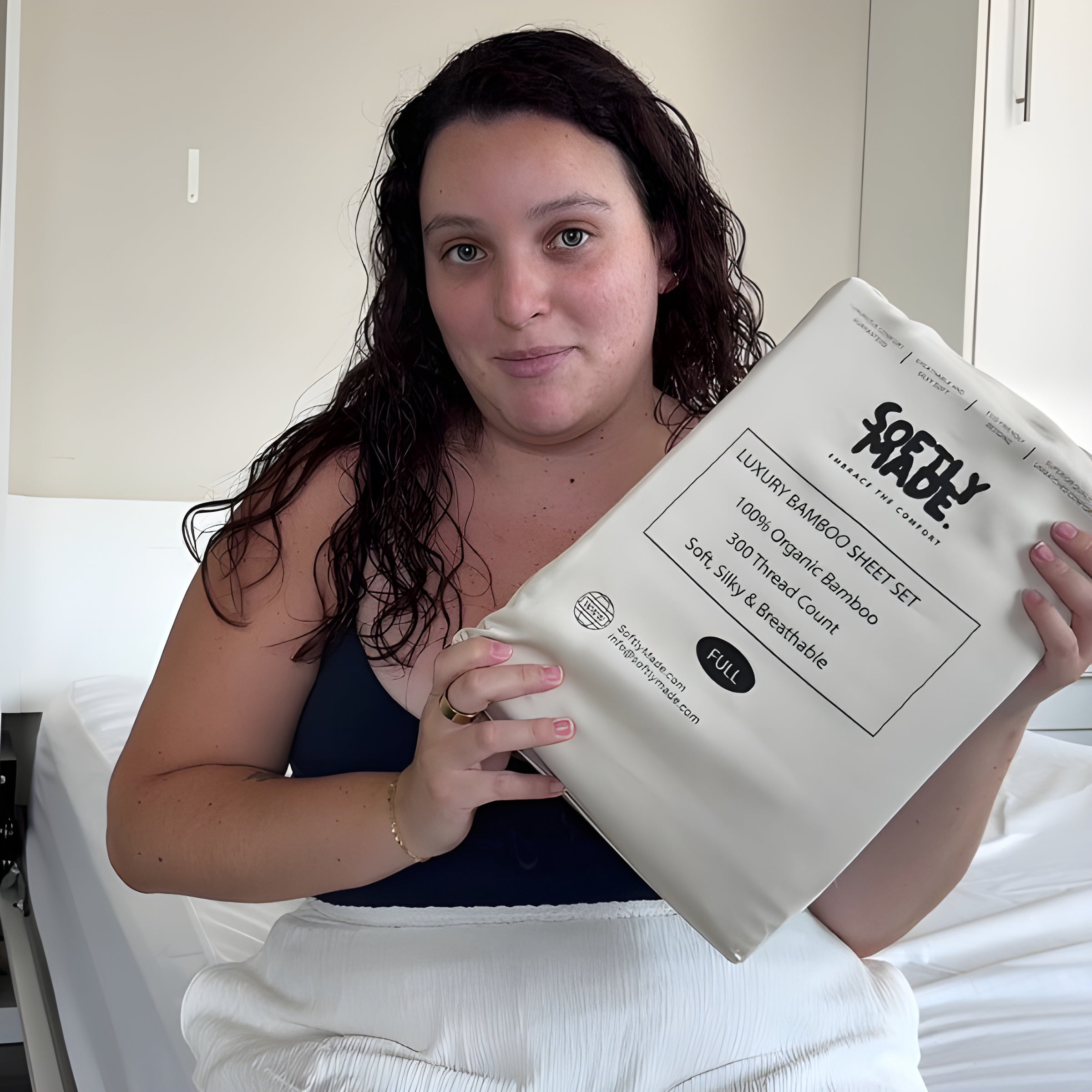 Woman holding a SoftlyMade branded luxury sheet set package in a bedroom setting
