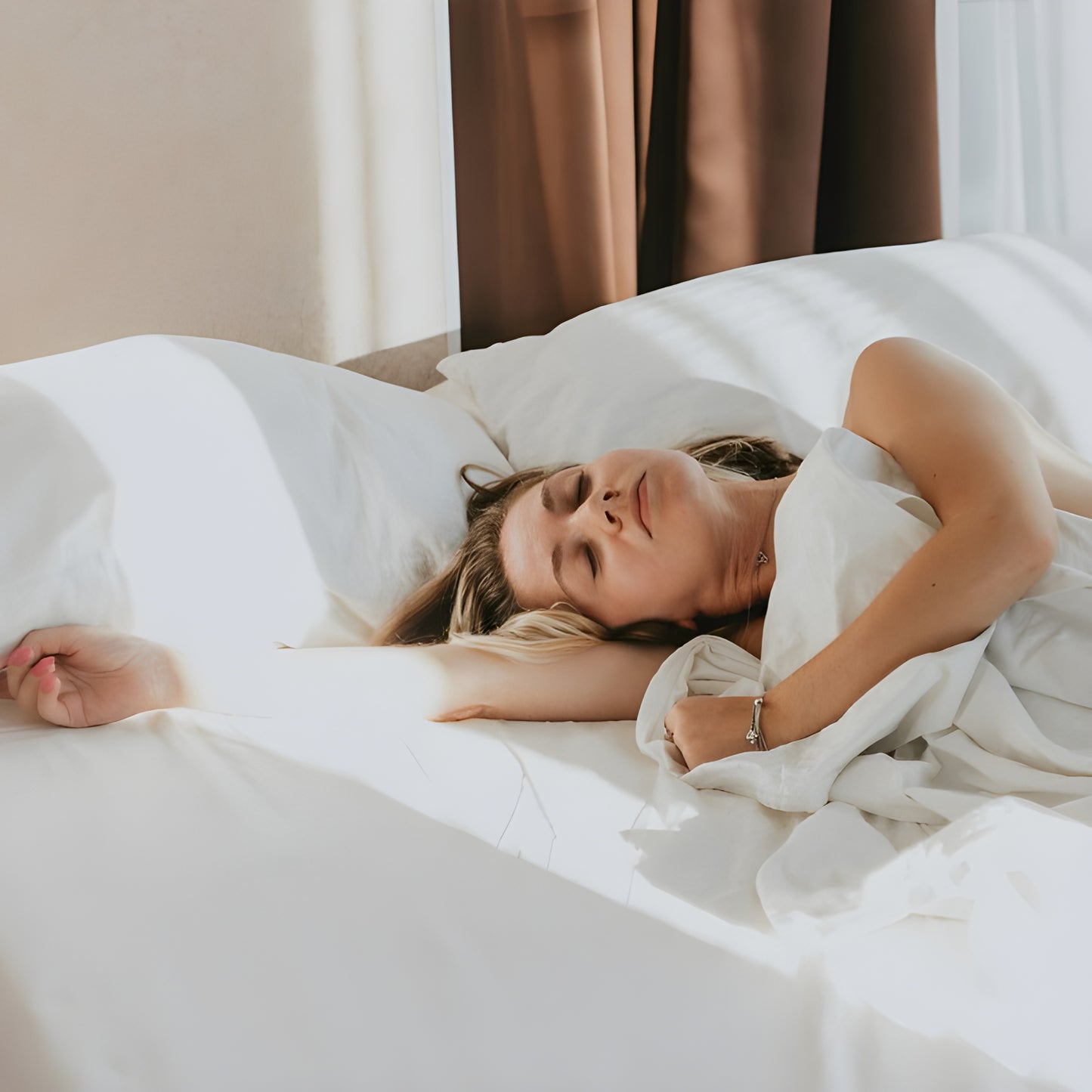 Woman lying in bed under white sheets with a neutral background