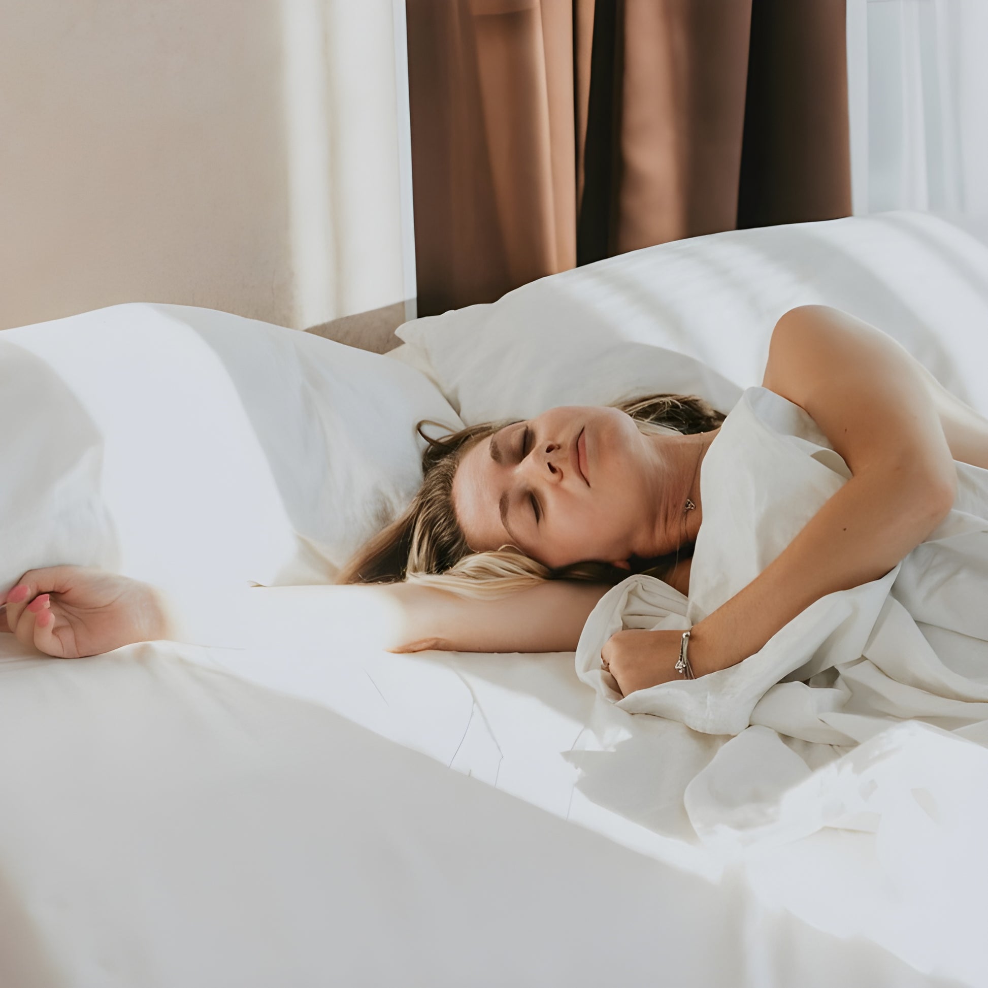 Woman lying in bed under white sheets with a neutral background