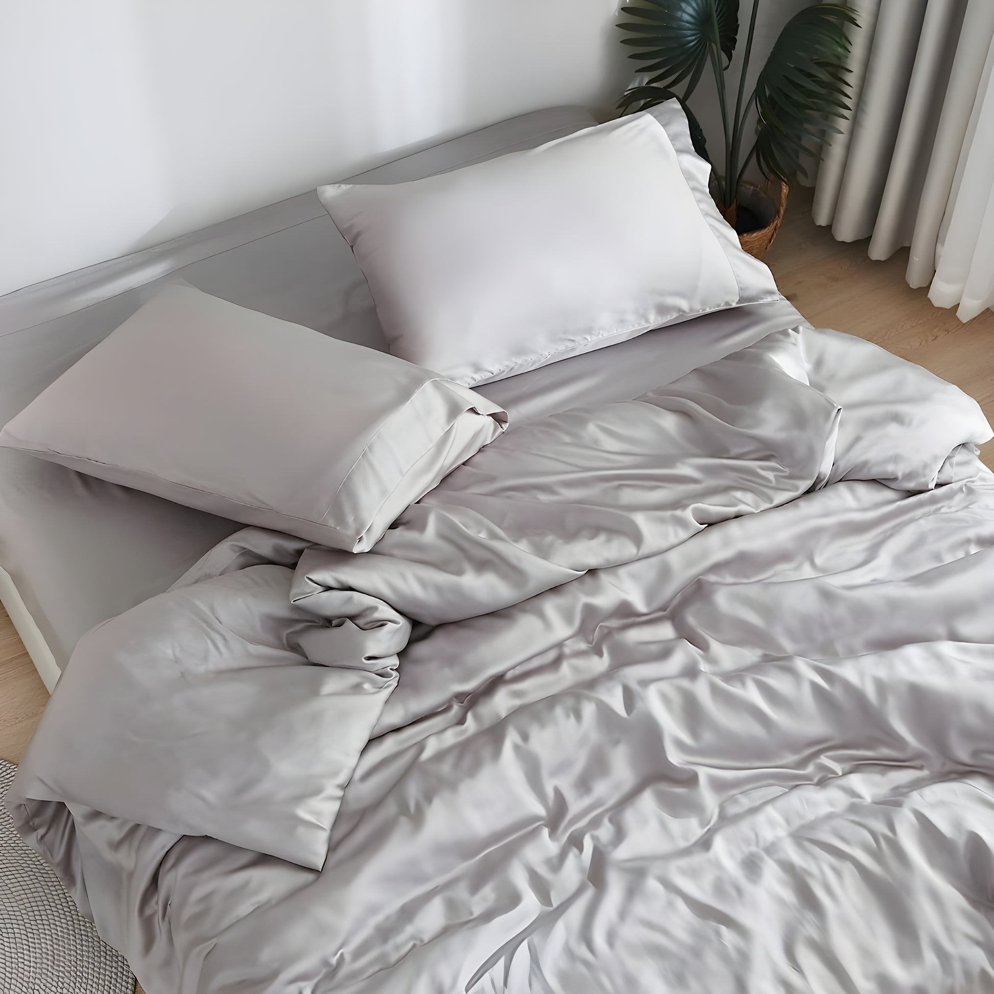 Luxurious gray bedding showcasing premium comfort with a person peacefully sleeping on soft sheets and pillows. The sleeper, wearing a light-colored top, appears comfortable and relaxed against the plush pillow and silky sheets, demonstrating the bedding's comfort benefits.