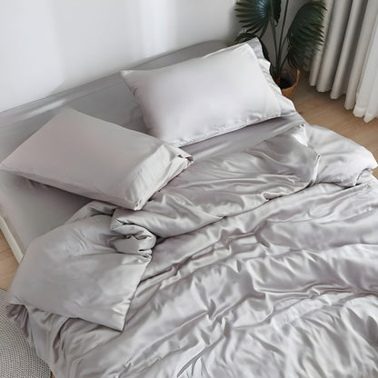 Luxurious gray bedding showcasing premium comfort with a person peacefully sleeping on soft sheets and pillows. The sleeper, wearing a light-colored top, appears comfortable and relaxed against the plush pillow and silky sheets, demonstrating the bedding's comfort benefits.